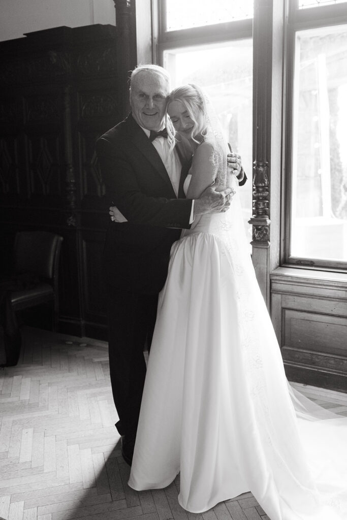 brides first look with dad in front of large windows with sunlight peaking in