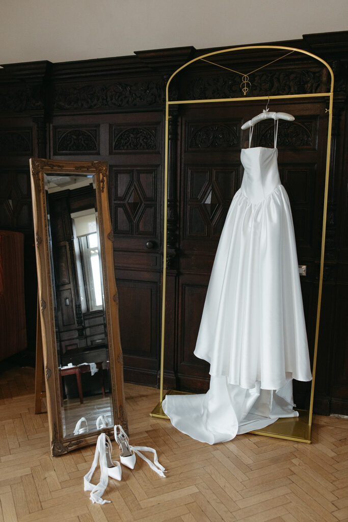 dress hanging on golden hanger next to mirror reflecting her shoes