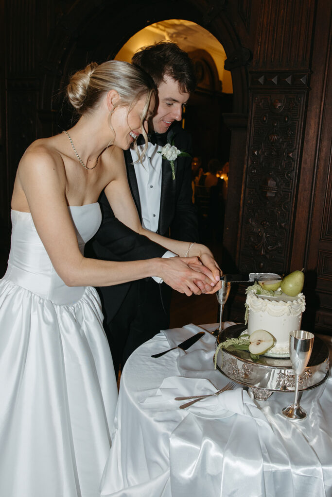 bride and groom cutting their pear cake, covered in pear and green accents